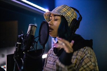 portrait of a woman wearing a cap singing in a microphone at a recording studio