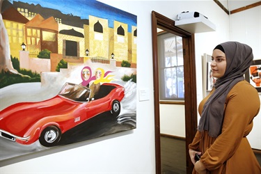 young woman looking at a painting of two women in a red car
