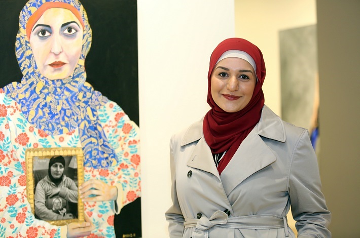 Amani Haydar smiling and posing next to her portrait