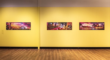 Photograph of three colourful artworks hung side-by-side on a yellow gallery wall