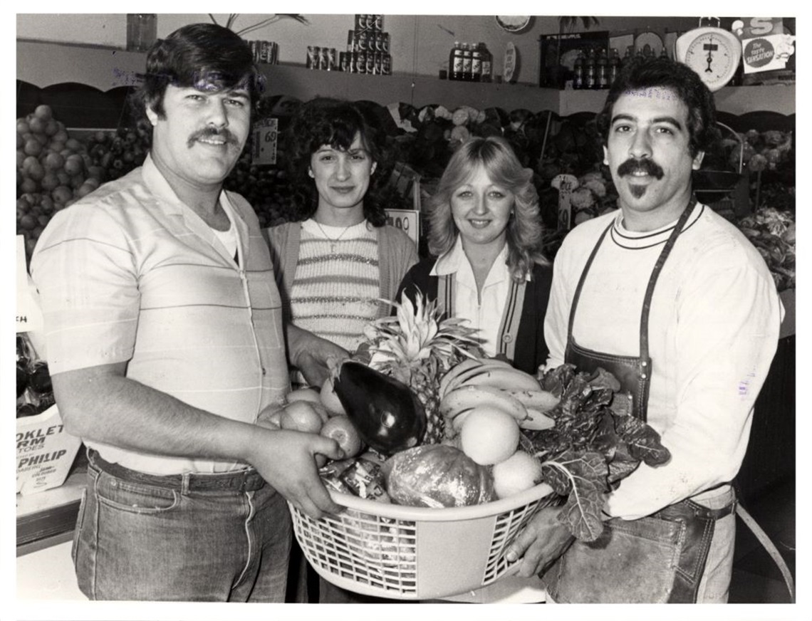 Two men holding a big basket of fruit in front of two women