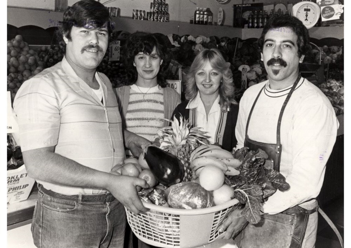 Two men holding a big basket of fruit in front of two women
