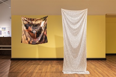Photograph and text printed on fabric suspended in a gallery with yellow walls