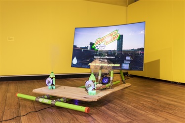Artwork installation featuring a large tv screen, mountain dew bottles and construction materials
