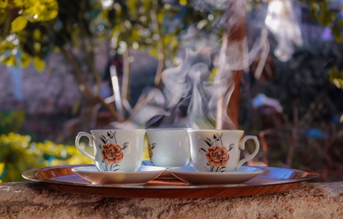 Three steaming cups of tea in front of scenic green background