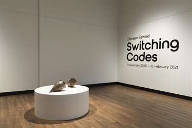 Exhibition installation view showing round plinth with two copper sculptures and text on the wall