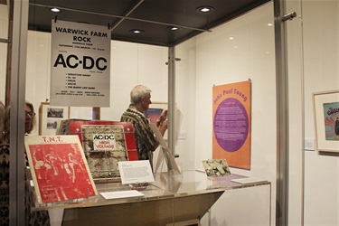 Museum display with AC-DC memorabilia, records, photographs and a visitor reading a wall text