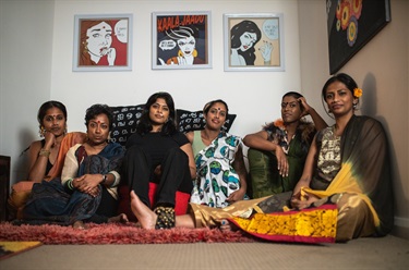 Group portrait of six women sitting next to each other on the floor of a room
