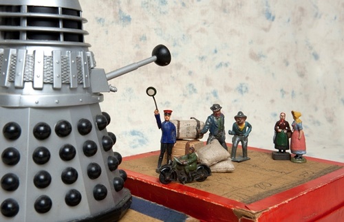 Group of toy miniature figurines of people standing on a box and facing a futuristic silver and black sculpture
