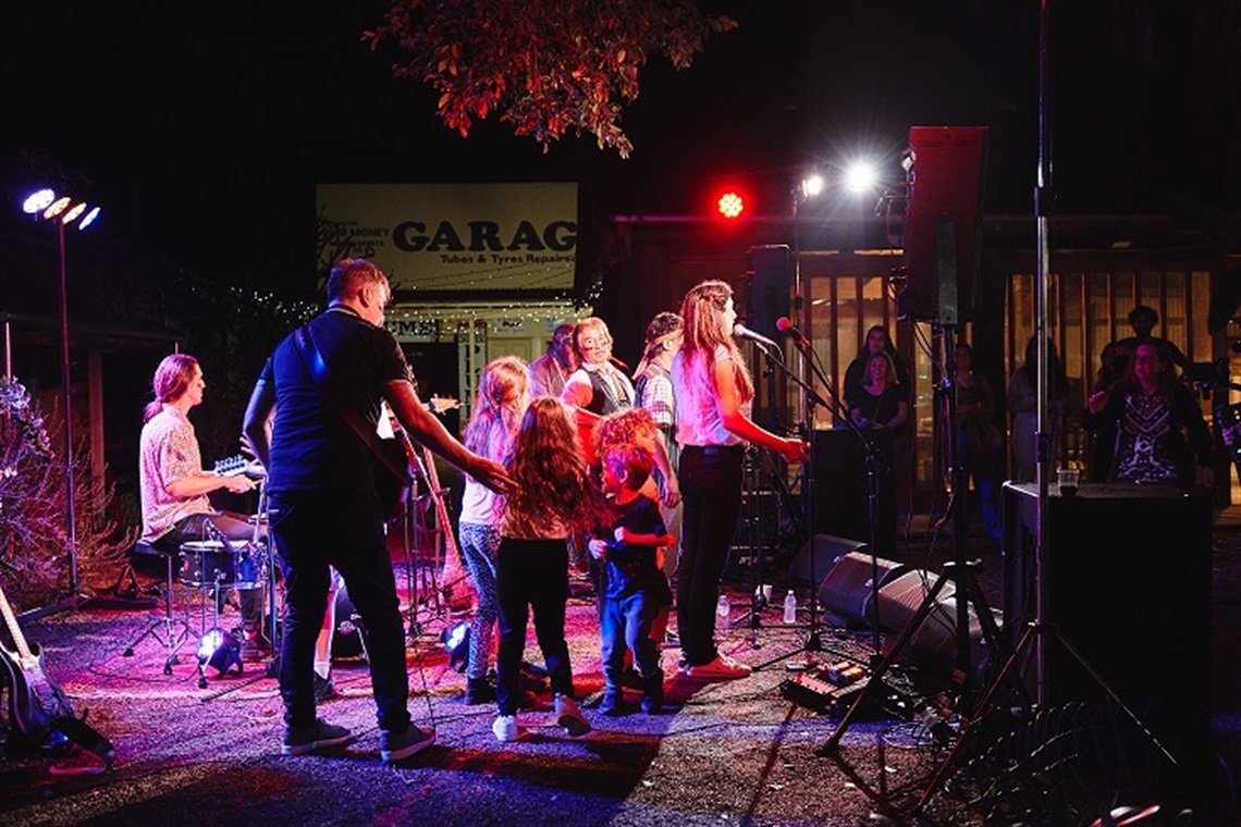 Worlds Collide band in FCMG Vintage Village, performing at night time. 